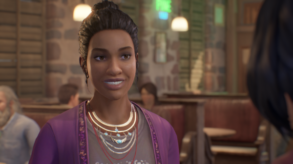 Screenshot of a smiling Charlotte Harmon in The Black Lantern. She is wearing multiple necklaces and a purple cardigan. Her hair is tied up into a bun, with loose strands hanging in front of her ears.