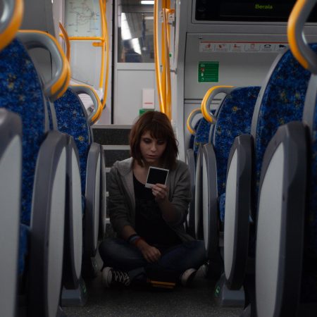 Max Caulfield cosplayer on a train, holding a Polaroid photograph. There is a Polaroid camera in front of her.