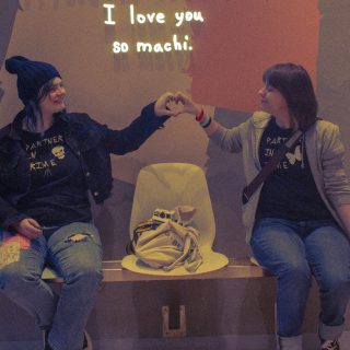 Max and Chloe holding their hands out to make a heart together, underneath a sign that says "I love you so machi". Max and Chloe are wearing matching shirts that says "Partner in Crime" (with a skull), and "Partner in Time" (with a butterfly).